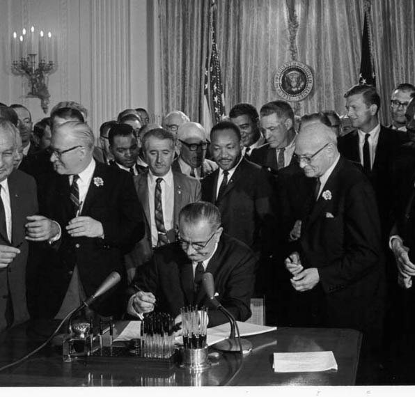 Martin Luther King Jr stands behind President Johnson as he signs the Civil Rights Act. 2nd July 1964